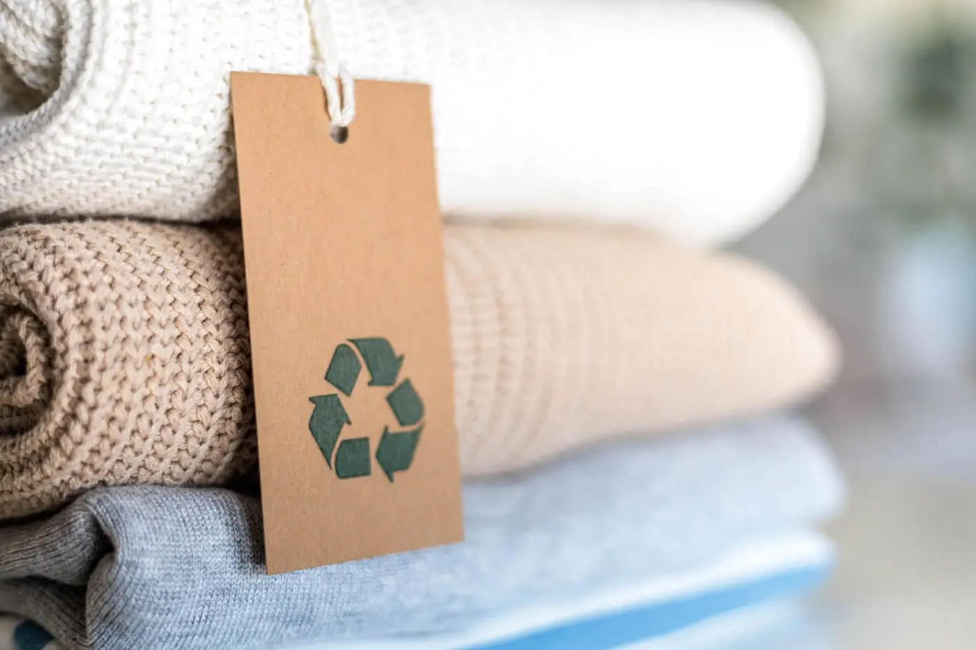 Knitted warm clothes neatly folded heap with craft tag recycling material circle arrow closeup